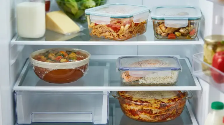 Contenitori con cibi cotti e avanzi conservati in frigorifero su più ripiani